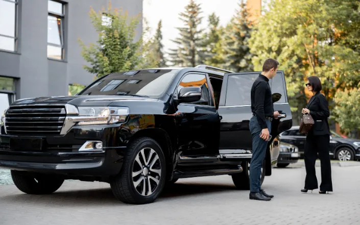 Chauffeur assisting a passenger into a black luxury SUV